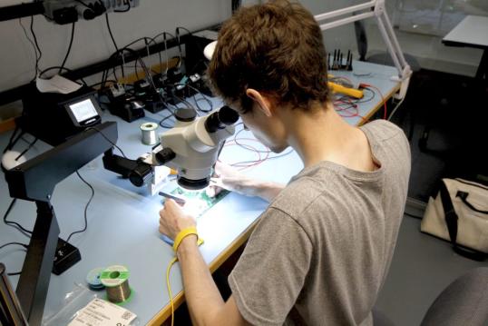 A young man seated in a laboratory, carefully examining something under a microscope.