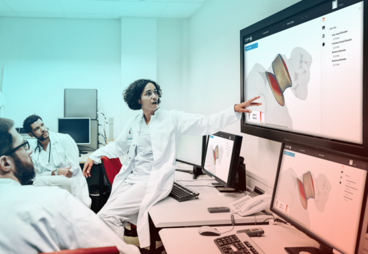 Researchers in white coats engaged in discussions while analyzing images displayed on a large monitor in a laboratory.