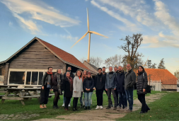 Group of people representing the winning city of Eeklo in front of a wooden house with a wind turbine in the background